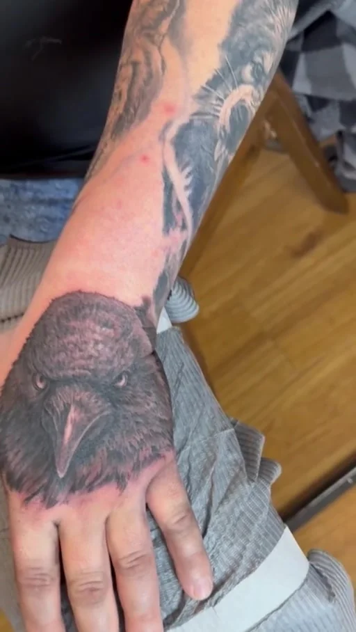 Dark bird head tattoo on the back of a hand